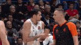 a basketball player wearing a real madrid jersey is talking to an umpire