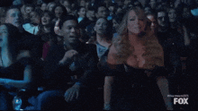 a woman in a black dress is sitting in a crowd at a fox show