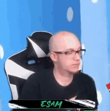 a bald man wearing glasses and a black shirt is sitting in a gaming chair .