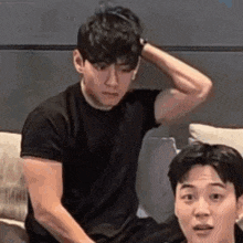 a man is sitting on a couch with his hand on his head and another man is sitting next to him .