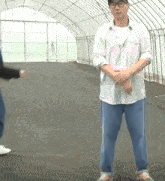 a man in a pink and white striped shirt and blue jeans stands in front of a greenhouse