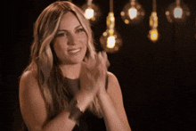 a woman is clapping her hands in front of a bunch of light bulbs