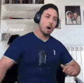 a man wearing headphones and a blue shirt is standing in front of a picture of a family .