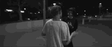 two people are standing next to each other in a black and white photo . one of the people is wearing a white shirt .