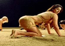 a woman in a bikini is crawling on the ground in the sand .