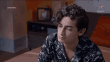 a young man with curly hair is sitting on a bed in front of a tv screen that says cerovillars