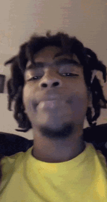 a man with dreadlocks is wearing a yellow shirt and making a face