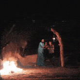 a man and a woman are standing in front of a fire at night