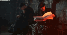 two men are sitting next to each other in a dark room reading newspapers .