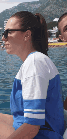 a woman wearing sunglasses and a blue and white shirt is sitting in the water