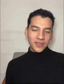 a young man wearing a black turtleneck is smiling and looking at the camera .
