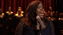 a woman singing into a microphone with a choir behind her