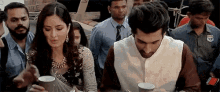 a man and a woman are sitting at a table drinking coffee from cups .