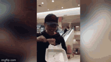 a man in a hat is holding a styrofoam container in a shopping mall