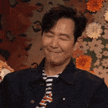 a man wearing a striped shirt and tie is smiling with his eyes closed in front of flowers .