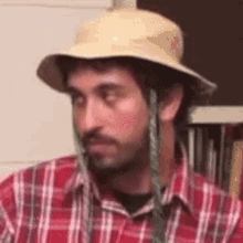 a man wearing a straw hat and a plaid shirt is sitting in a room .