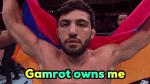 a shirtless man is holding a colorful flag with the words gamrot owns me above him