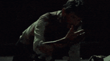 a man in a bloody shirt is crawling on the floor holding another man 's arm .