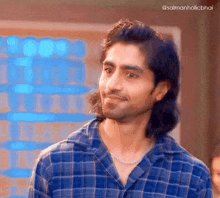 a man with long hair and a plaid shirt is smiling and looking at the camera .
