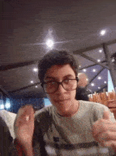 a young man wearing glasses and a green shirt is giving a thumbs up