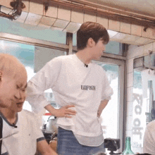 a man wearing a white uniform t-shirt is standing in a room with other people .