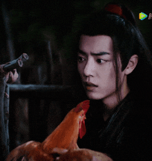 a man with long hair is holding a chicken and looking at it