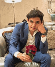 a man in a suit and tie is sitting on a couch holding a bouquet of flowers .