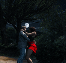 a man and a woman are hugging under a tree with a full moon in the background