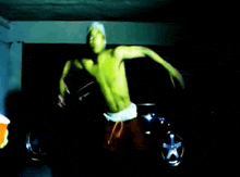 a shirtless man is dancing in a dark room with a car in the background