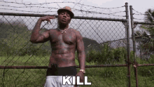a man without a shirt is standing in front of a chain link fence holding a gun and the word kill is above him .