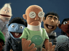 a group of puppets including one wearing glasses and a green shirt with a smiling face on it