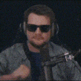 a man wearing sunglasses and headphones is standing in front of a microphone and making a funny face .