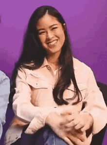 a woman is smiling while sitting in a chair with her hands folded .