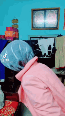 a woman wearing a pink sweater and a head scarf is standing in a room with clothes hanging on a rack .