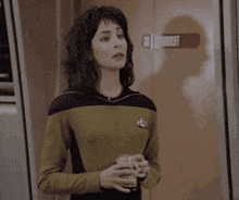 a woman in a star trek uniform holds a glass in her hands