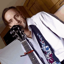 a man in a white shirt and tie is holding an ibanez guitar