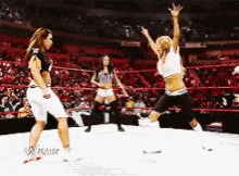 three women are wrestling in a wrestling ring with a referee in the background