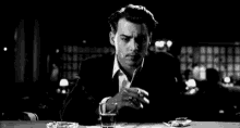 a man is smoking a cigarette and drinking a glass of whiskey .