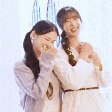 two women are standing next to each other in front of a window and smiling .
