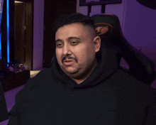 a man in a black hoodie is sitting in a gaming chair with his eyes closed