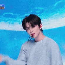 a young man wearing a light blue sweater and a microphone is standing in front of a blue background .