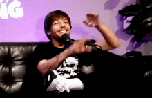 a man is sitting on a couch with a microphone in front of him .