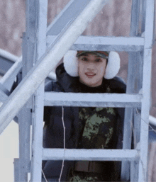 a man wearing ear muffs and a hat is standing on a ladder