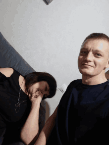 a man and a woman are sitting on a couch and the woman is covering her face with her hand