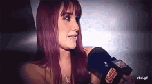 a woman with long red hair is talking into a microphone that says rbd.gif on it