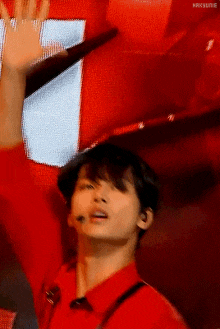 a man in a red shirt is waving his hand in the air while standing on a stage .