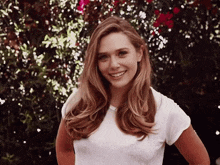 a woman wearing a white shirt is smiling in front of a bush