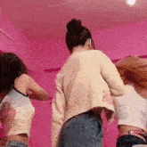 three women are standing next to each other in a room with a pink wall .