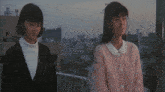 two women are standing next to each other with a city in the background