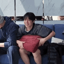 a man and a woman are sitting on a couch holding a red pillow .